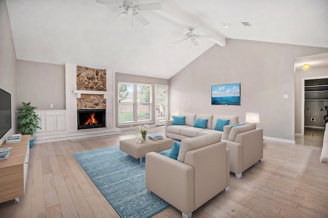 living room featuring beam ceiling, light hardwood / wood-style floors, a stone fireplace, and ceiling fan