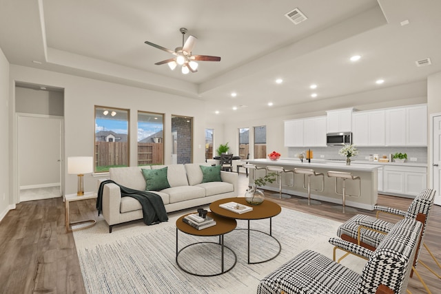 living room featuring a tray ceiling, light hardwood / wood-style floors, ceiling fan, and sink