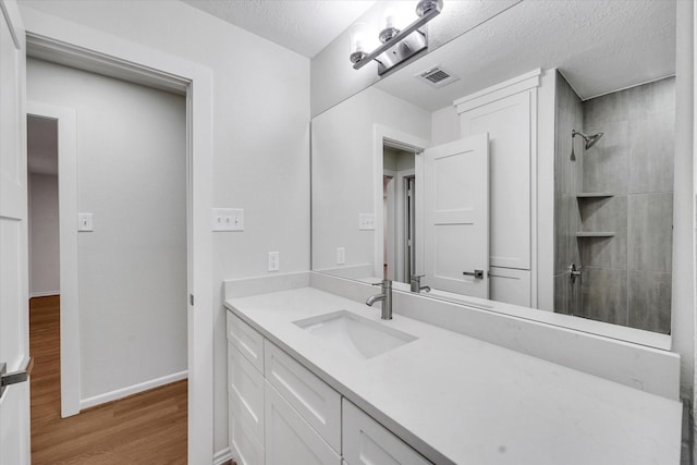 bathroom featuring tiled shower, wood-type flooring, vanity, and a textured ceiling