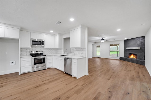 kitchen with sink, white cabinetry, stainless steel appliances, light hardwood / wood-style floors, and a brick fireplace