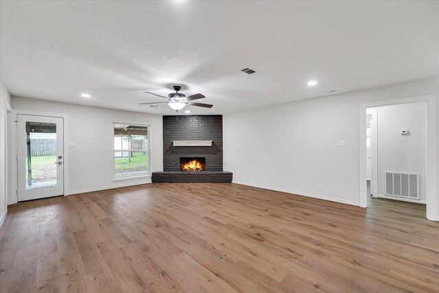 unfurnished living room featuring ceiling fan, a brick fireplace, and light hardwood / wood-style floors