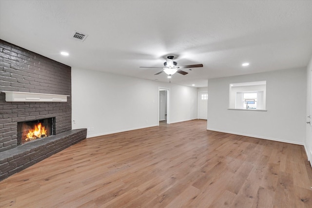 unfurnished living room featuring ceiling fan, light hardwood / wood-style floors, and a brick fireplace