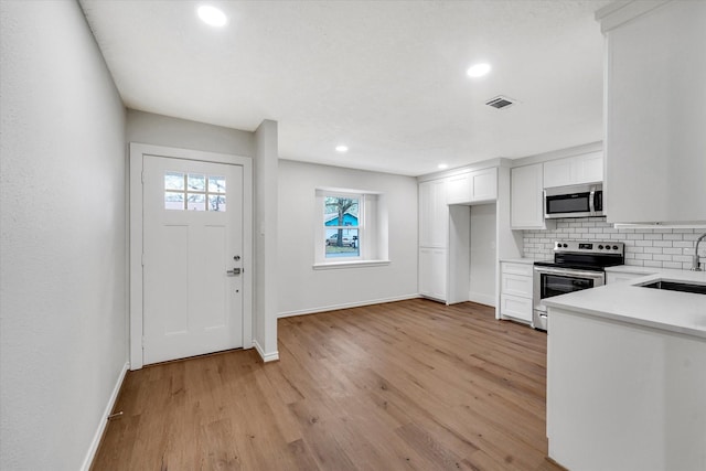 kitchen with sink, appliances with stainless steel finishes, tasteful backsplash, light hardwood / wood-style floors, and white cabinets