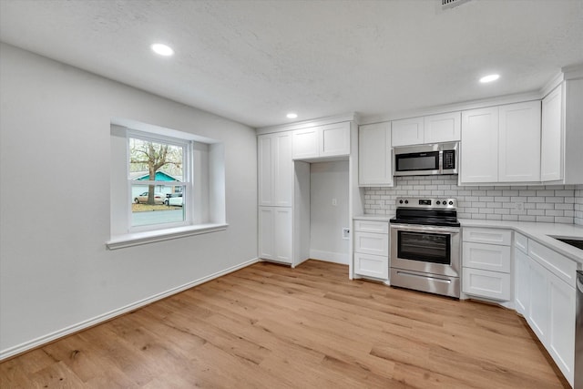 kitchen featuring white cabinetry, backsplash, stainless steel appliances, light hardwood / wood-style floors, and a textured ceiling