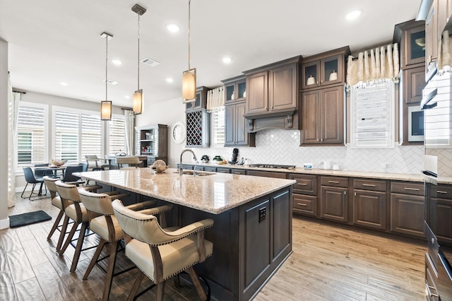 kitchen featuring light hardwood / wood-style flooring, a center island with sink, sink, backsplash, and decorative light fixtures