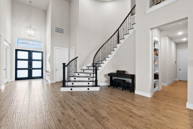 foyer entrance with french doors, hardwood / wood-style floors, and a towering ceiling