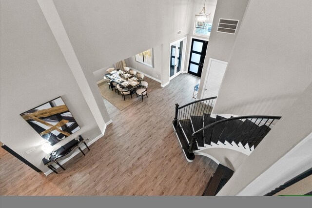 staircase with light wood-type flooring, a notable chandelier, and a towering ceiling