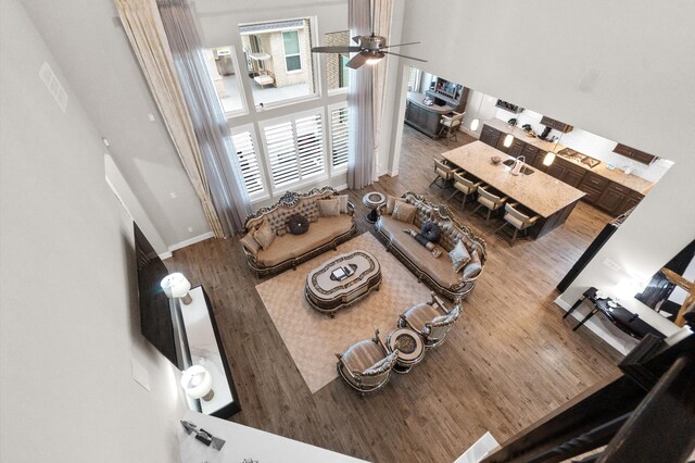 living room with wood-type flooring, ceiling fan, and a towering ceiling