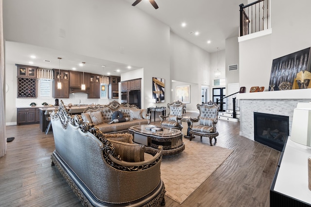 living room with sink, a tiled fireplace, dark hardwood / wood-style flooring, ceiling fan, and a towering ceiling