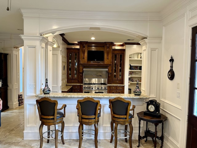 bar with light tile patterned floors, light stone countertops, double oven range, and decorative columns