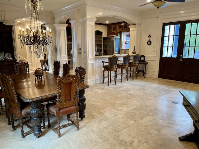 tiled dining room featuring ceiling fan with notable chandelier, french doors, ornate columns, and ornamental molding