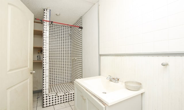 bathroom with vanity, a tile shower, a textured ceiling, and tile patterned flooring