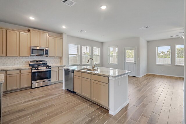 kitchen with sink, appliances with stainless steel finishes, backsplash, and a kitchen island with sink