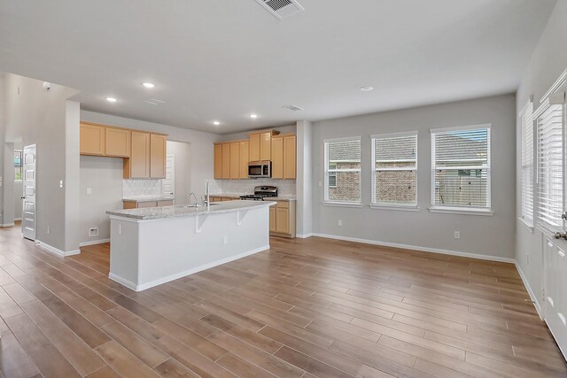 kitchen featuring light brown cabinets, light wood-type flooring, a kitchen island with sink, appliances with stainless steel finishes, and decorative backsplash