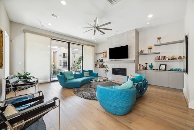 living room with a fireplace, light wood-type flooring, and ceiling fan