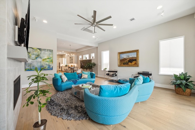 living room featuring light hardwood / wood-style flooring, a tile fireplace, and ceiling fan with notable chandelier