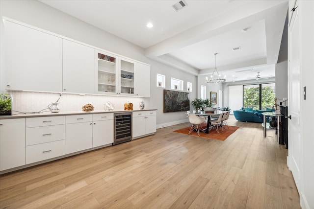 kitchen with light hardwood / wood-style flooring, decorative light fixtures, beverage cooler, white cabinets, and tasteful backsplash