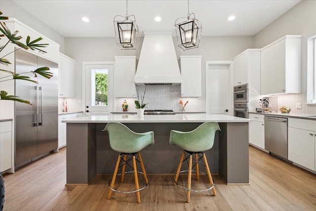 kitchen with white cabinetry, light wood-type flooring, appliances with stainless steel finishes, and premium range hood