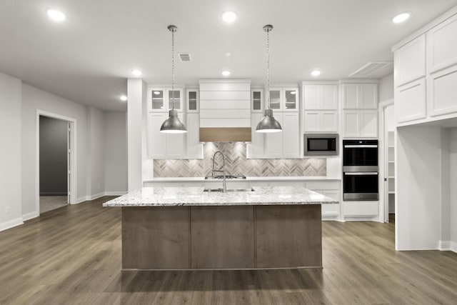 kitchen featuring built in microwave, a center island with sink, and white cabinets