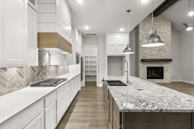 kitchen with decorative light fixtures, a center island with sink, a fireplace, white cabinetry, and stainless steel gas stovetop