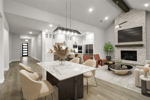 dining space featuring a stone fireplace, ceiling fan, lofted ceiling with beams, and hardwood / wood-style flooring