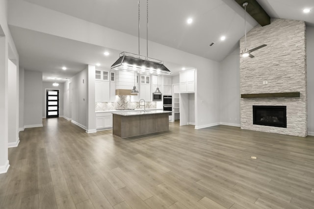 kitchen featuring beam ceiling, white cabinetry, an island with sink, decorative light fixtures, and a fireplace