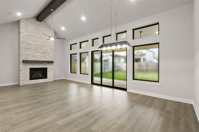 unfurnished living room with beam ceiling, a stone fireplace, ceiling fan, and hardwood / wood-style floors