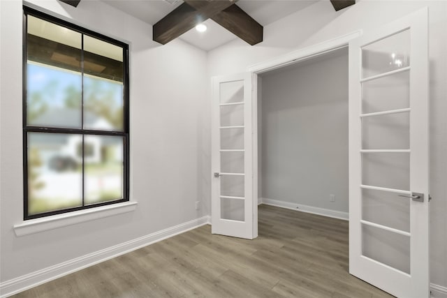 empty room featuring beamed ceiling, french doors, and hardwood / wood-style flooring