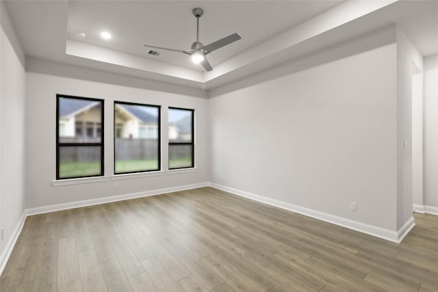 unfurnished room featuring a raised ceiling, ceiling fan, and light hardwood / wood-style floors