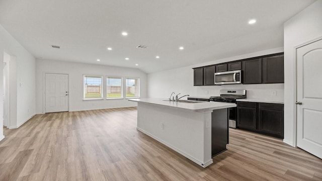 kitchen with appliances with stainless steel finishes, light wood-type flooring, a kitchen island with sink, and sink