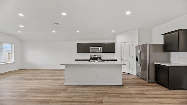 kitchen with stainless steel appliances, sink, light hardwood / wood-style floors, lofted ceiling, and an island with sink