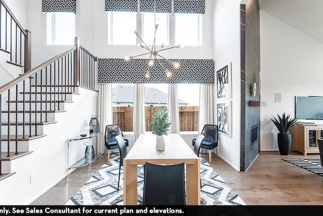 dining room with a tile fireplace, a towering ceiling, a chandelier, and light hardwood / wood-style floors