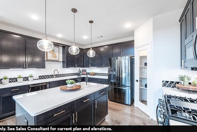 kitchen with tasteful backsplash, decorative light fixtures, appliances with stainless steel finishes, a kitchen island, and light hardwood / wood-style floors