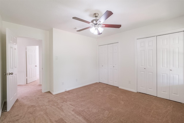 unfurnished bedroom featuring light carpet, two closets, and ceiling fan