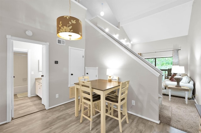 dining area with high vaulted ceiling, beam ceiling, and light hardwood / wood-style floors