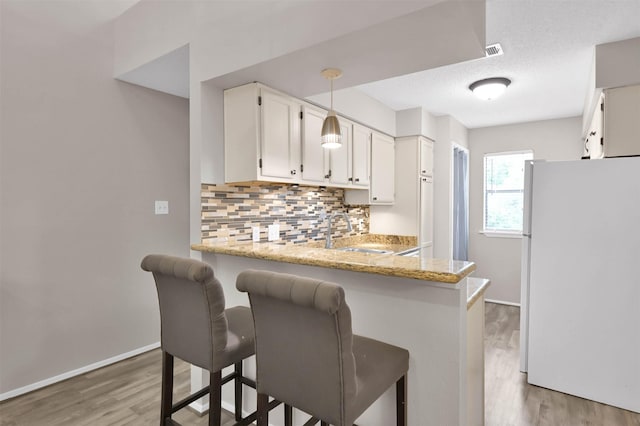 kitchen featuring a breakfast bar, sink, decorative backsplash, white fridge, and kitchen peninsula