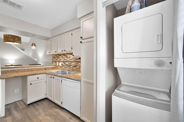 kitchen featuring stacked washer and clothes dryer, white dishwasher, sink, and white cabinets