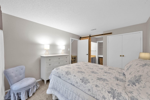 bedroom with connected bathroom, a barn door, light carpet, a textured ceiling, and a closet