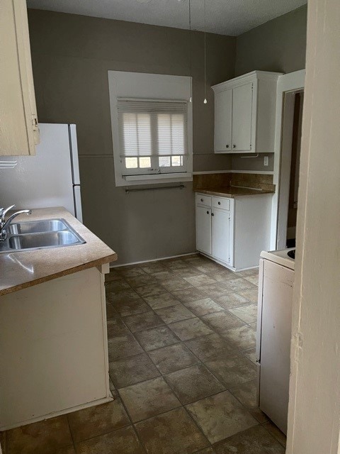 kitchen featuring sink, white fridge, dark tile patterned floors, and white cabinets