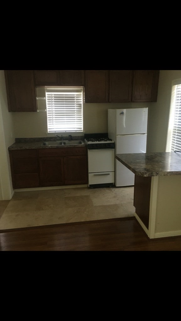 kitchen with dark brown cabinetry, sink, hardwood / wood-style flooring, and white appliances