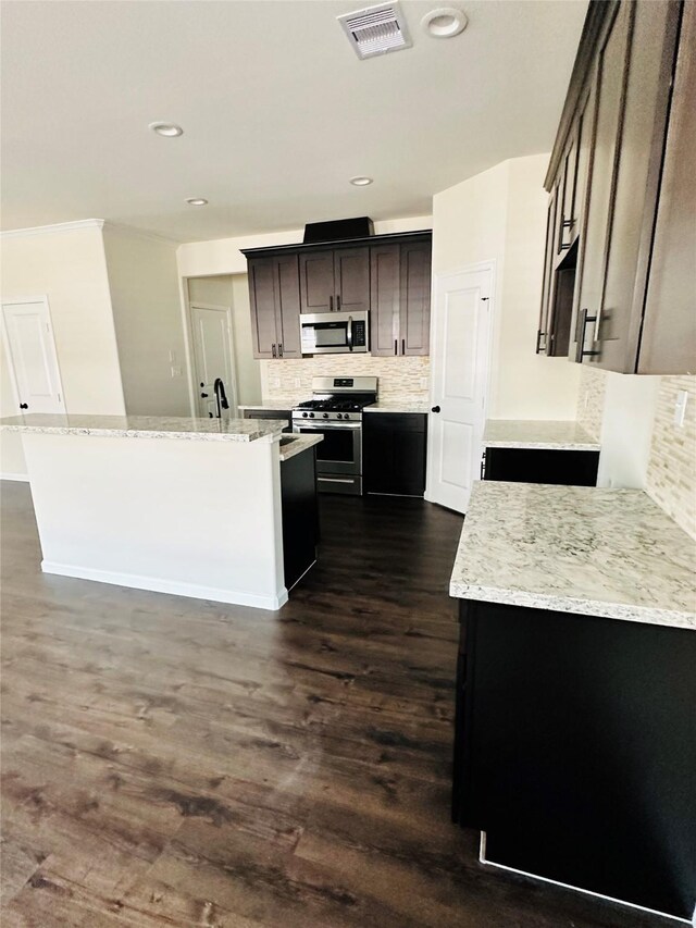 kitchen featuring a center island, dark wood-type flooring, light stone counters, stainless steel appliances, and decorative backsplash