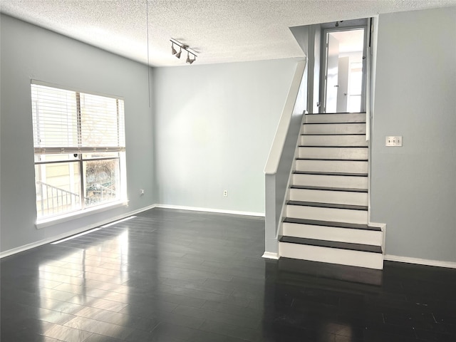 staircase with dark hardwood / wood-style floors, a textured ceiling, and track lighting