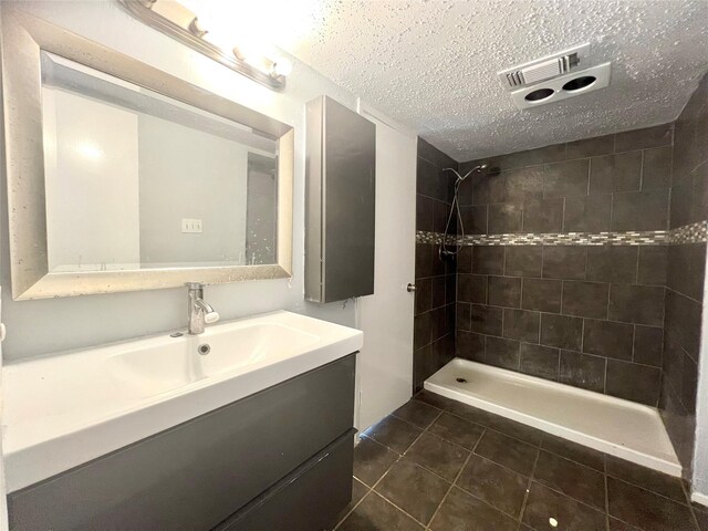 bathroom with vanity, a textured ceiling, a tile shower, and tile patterned floors