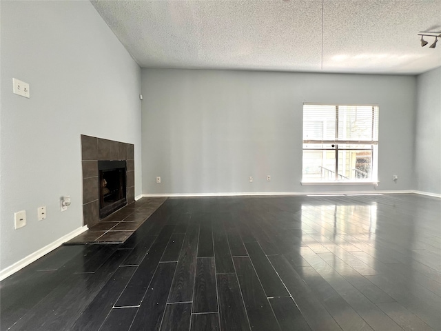 unfurnished living room with dark hardwood / wood-style floors, a tiled fireplace, and a textured ceiling