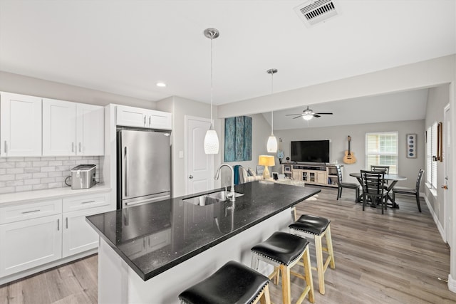 kitchen featuring ceiling fan, sink, a center island with sink, light hardwood / wood-style floors, and stainless steel refrigerator