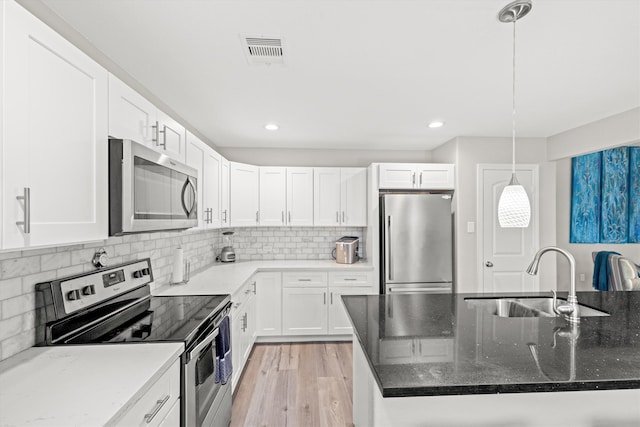 kitchen featuring appliances with stainless steel finishes, light hardwood / wood-style flooring, pendant lighting, dark stone countertops, and white cabinetry