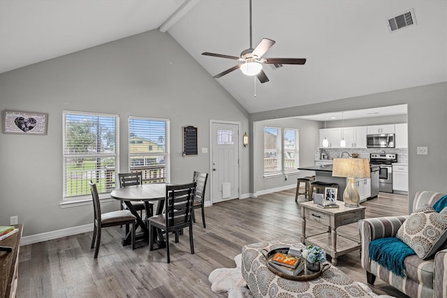 dining area with high vaulted ceiling, beamed ceiling, ceiling fan, and light hardwood / wood-style floors