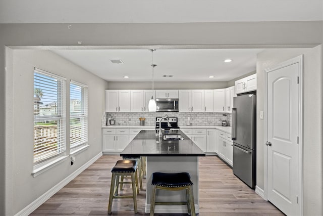 kitchen with tasteful backsplash, light wood-type flooring, white cabinets, a kitchen island with sink, and appliances with stainless steel finishes