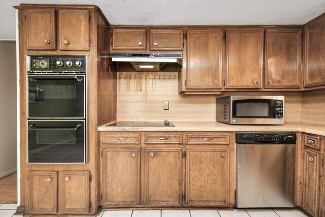 kitchen featuring light tile patterned flooring, tasteful backsplash, black appliances, and wall chimney exhaust hood