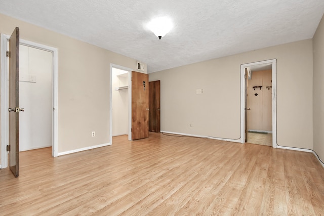 unfurnished bedroom featuring a spacious closet, a closet, ensuite bath, light wood-type flooring, and a textured ceiling